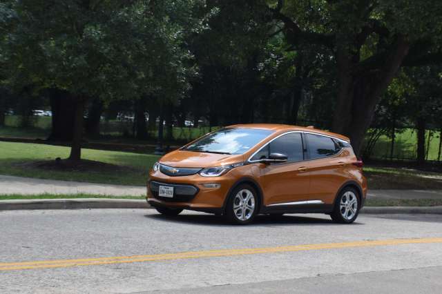 An orange electric car parked on the side of the street near a park.