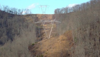 Power lines traverse a hillside with sparse vegetation and bare trees.