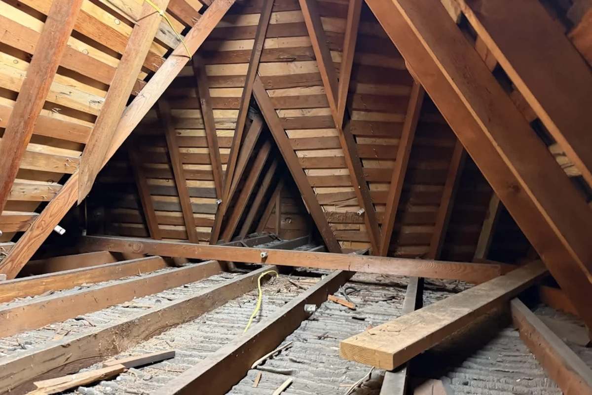 The interior of an attic with wooden beams and exposed floorboards.