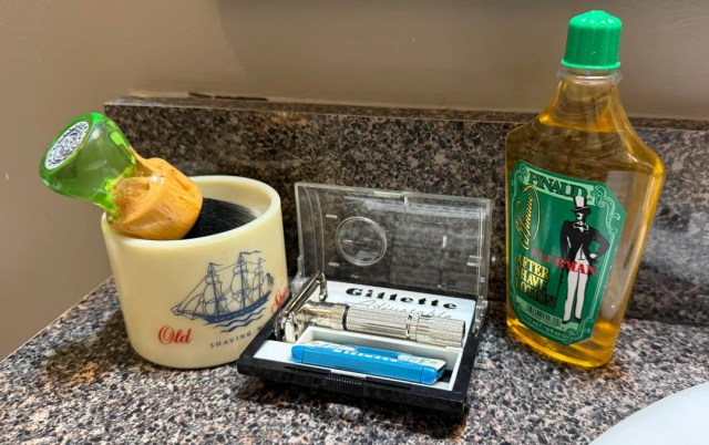 The razer next to a shaving brush and aftershave.