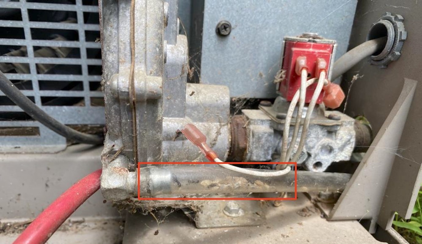 A close-up of a mechanical component with wires, a valve, and visible dirt and debris.