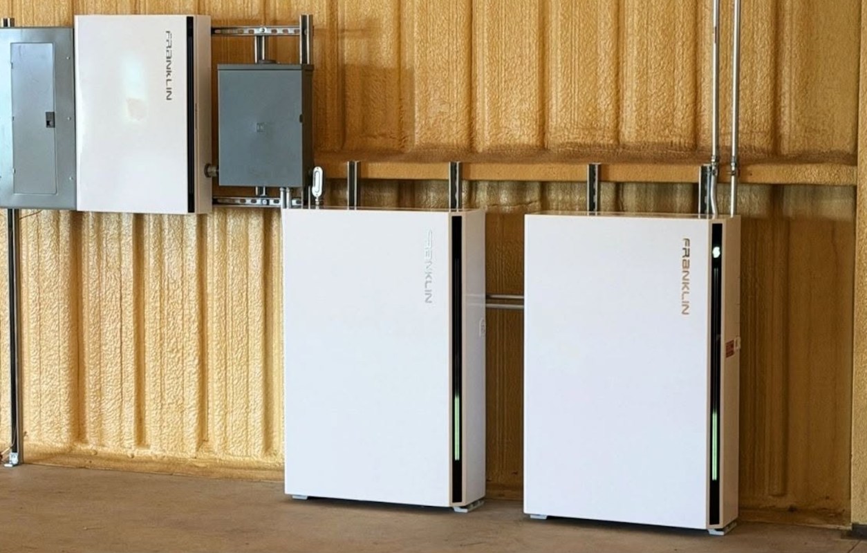 Two white electric boxes mounted on a wall next to a gray electrical panel in an indoor setting.