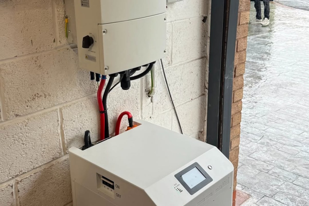 A wall-mounted inverter and battery unit connected by cables in a building.