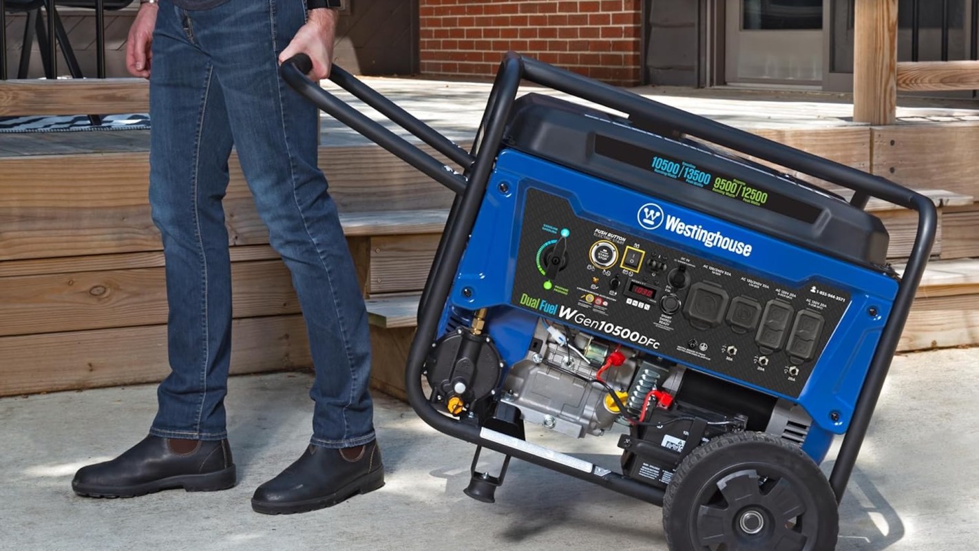 A person wheels a Westinghouse dual fuel generator across a concrete surface near a wooden deck.