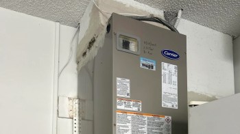 A gray heating unit mounted on a wall with visible specifications and a warning label.