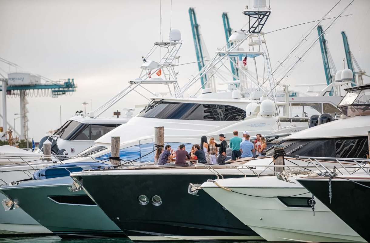 A group of people socializes on a dock among several large yachts.
