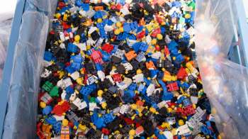 A large assortment of colorful LEGO minifigure parts in a container.