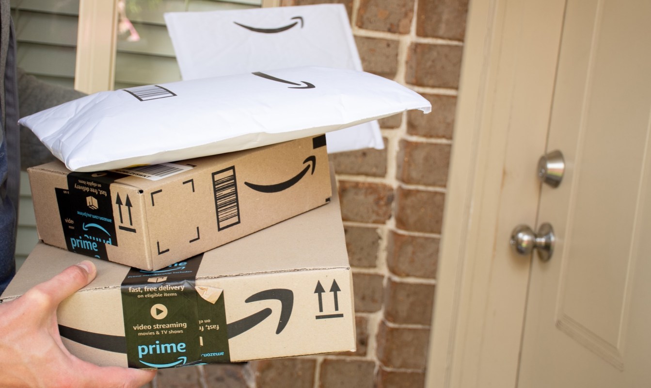 A person holds multiple Amazon packages at a doorstep.