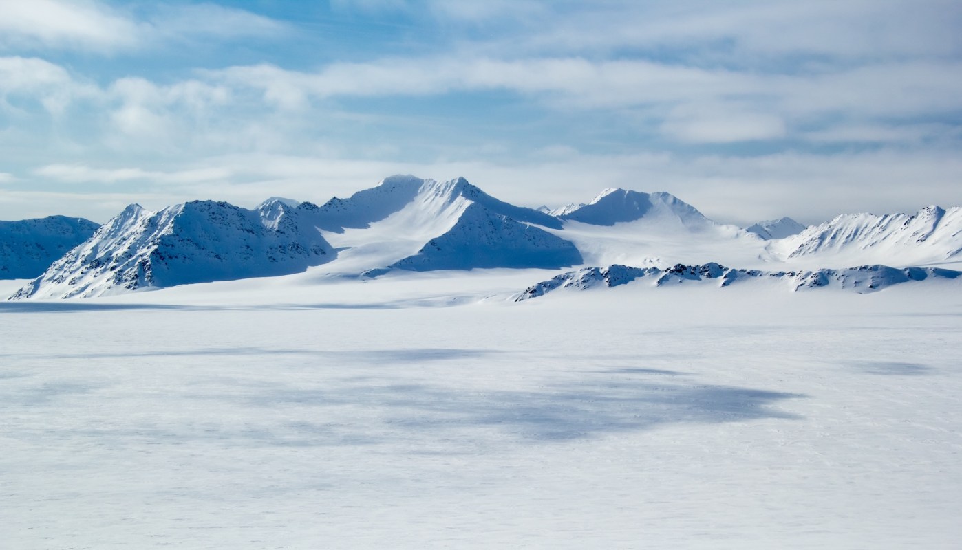 Snow-covered mountains under a partly cloudy sky with a vast glacier in the foreground.