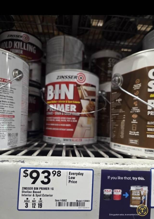 A shelf displaying a price tag for Zinsser Bin Primer with various paint cans in the background.