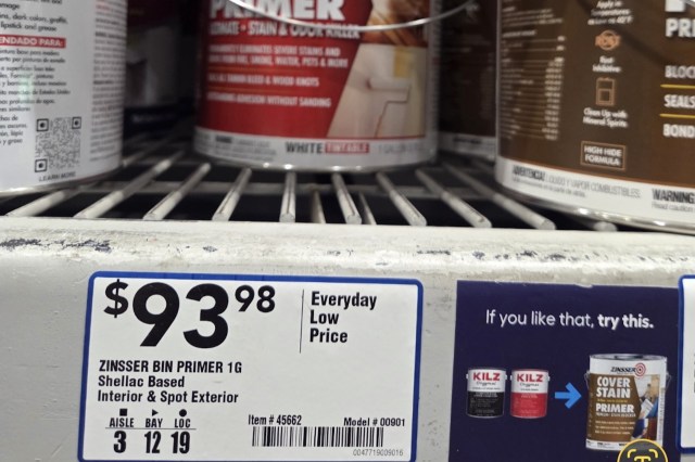 A shelf displaying a price tag for Zinsser Bin Primer with various paint cans in the background.