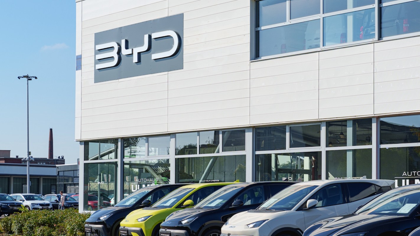 A row of parked cars in front of a building with a BYD sign.