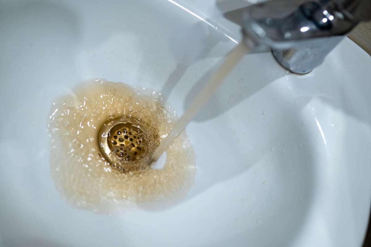 Water flows from a faucet into a sink, creating bubbles and discolored water around the drain.