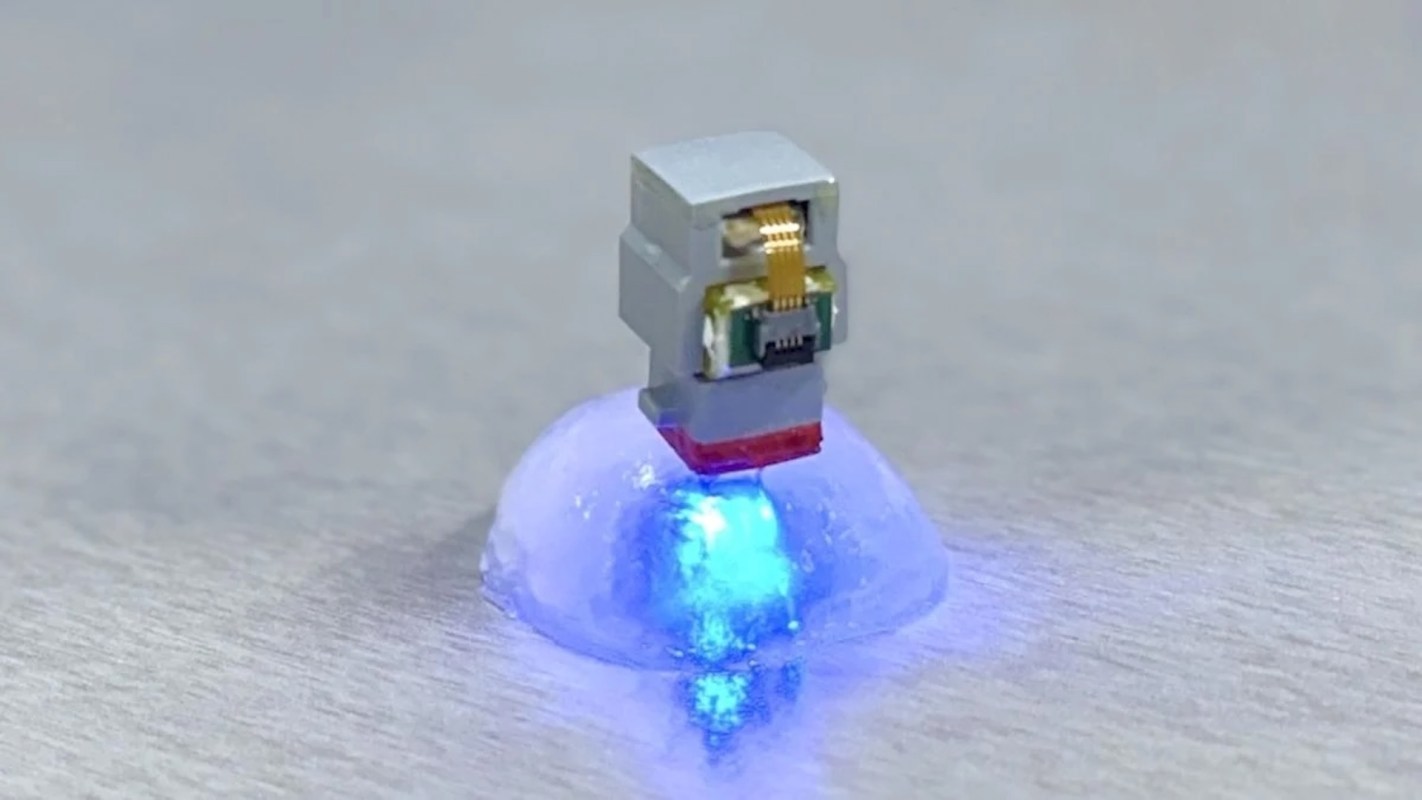A small electronic device emitting blue light while positioned on a translucent, dome-shaped object.