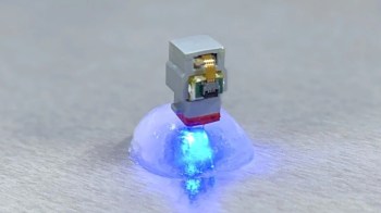 A small electronic device emitting blue light while positioned on a translucent, dome-shaped object.