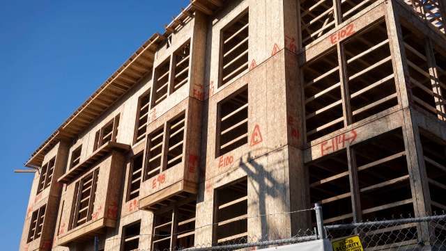 A partially constructed building with exposed wooden frames and marked measurements against a clear blue sky.