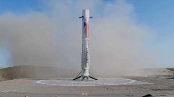 A rocket stands on a landing pad amid dust clouds in a barren landscape.