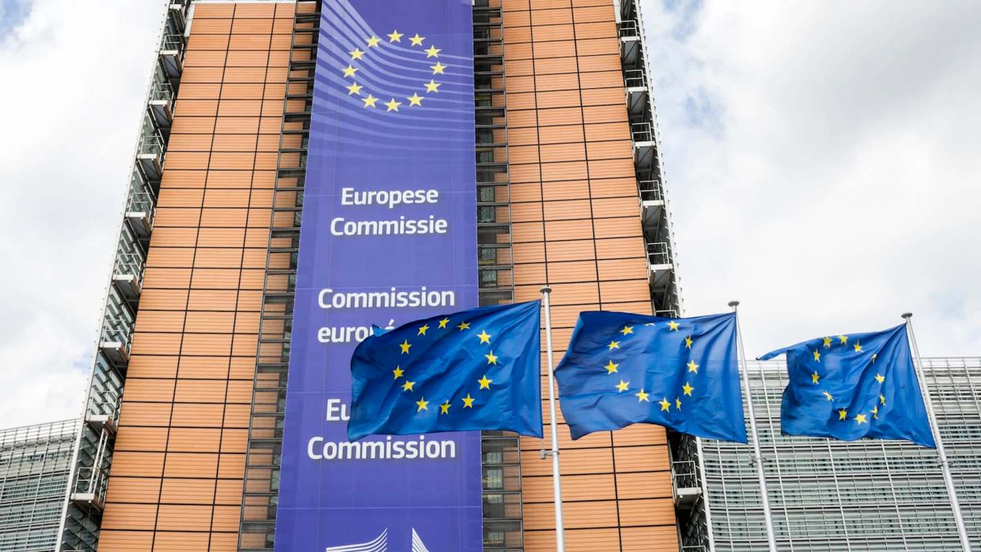 The European Commission building with EU flags in front and a banner displaying "European Commission."
