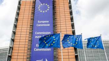 The European Commission building with EU flags in front and a banner displaying "European Commission."