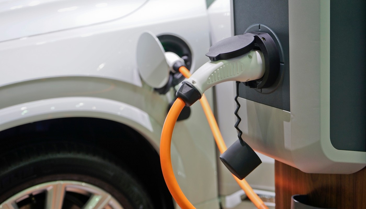 An electric vehicle charging at a charging station with an orange cable connected.