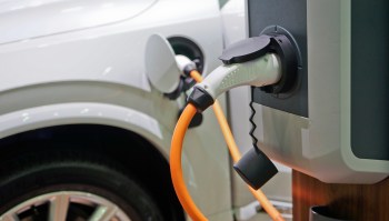 An electric vehicle charging at a charging station with an orange cable connected.