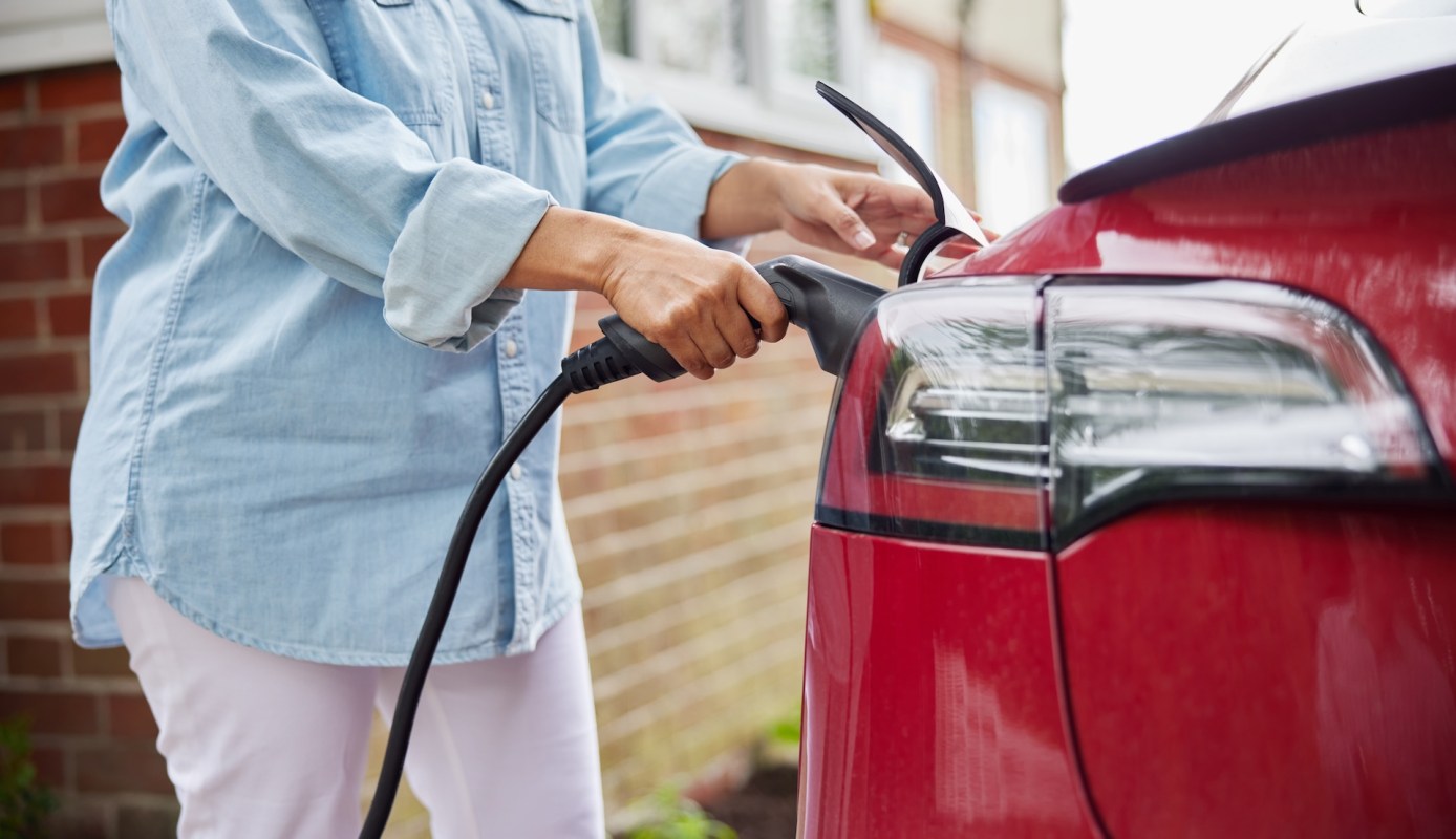 A person charges an electric vehicle using a charging cable at home.