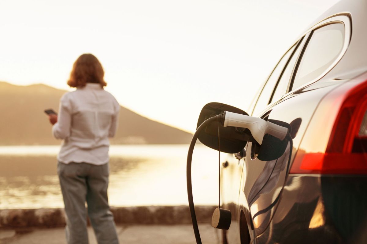 A woman stands in the distance while her electric vehicle charges