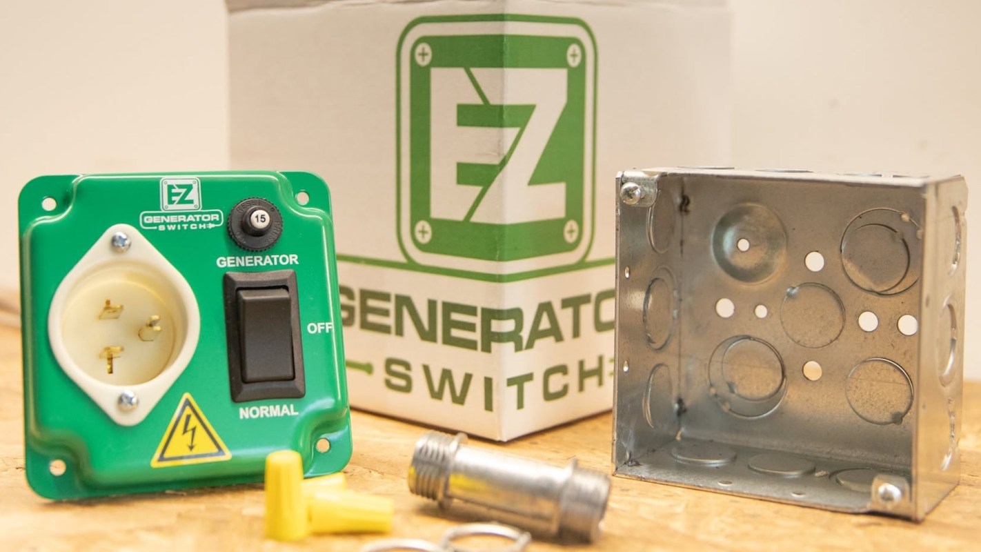 A green generator switch and a metal electrical box are displayed on a wooden surface with a branded box in the background.