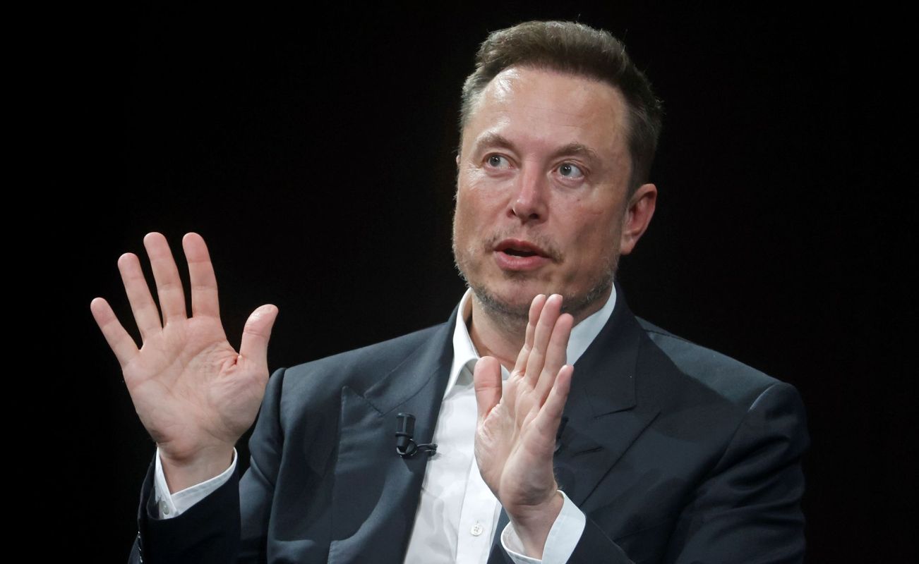 Elon Musk talks and gestures with his hands open and palms out