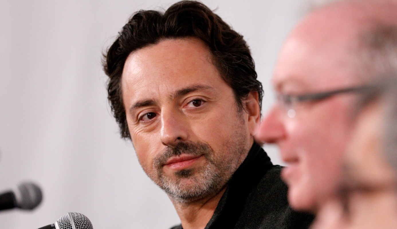 Google co-founder Sergey Brin speaks at a panel discussion, with another person partially visible in the foreground.