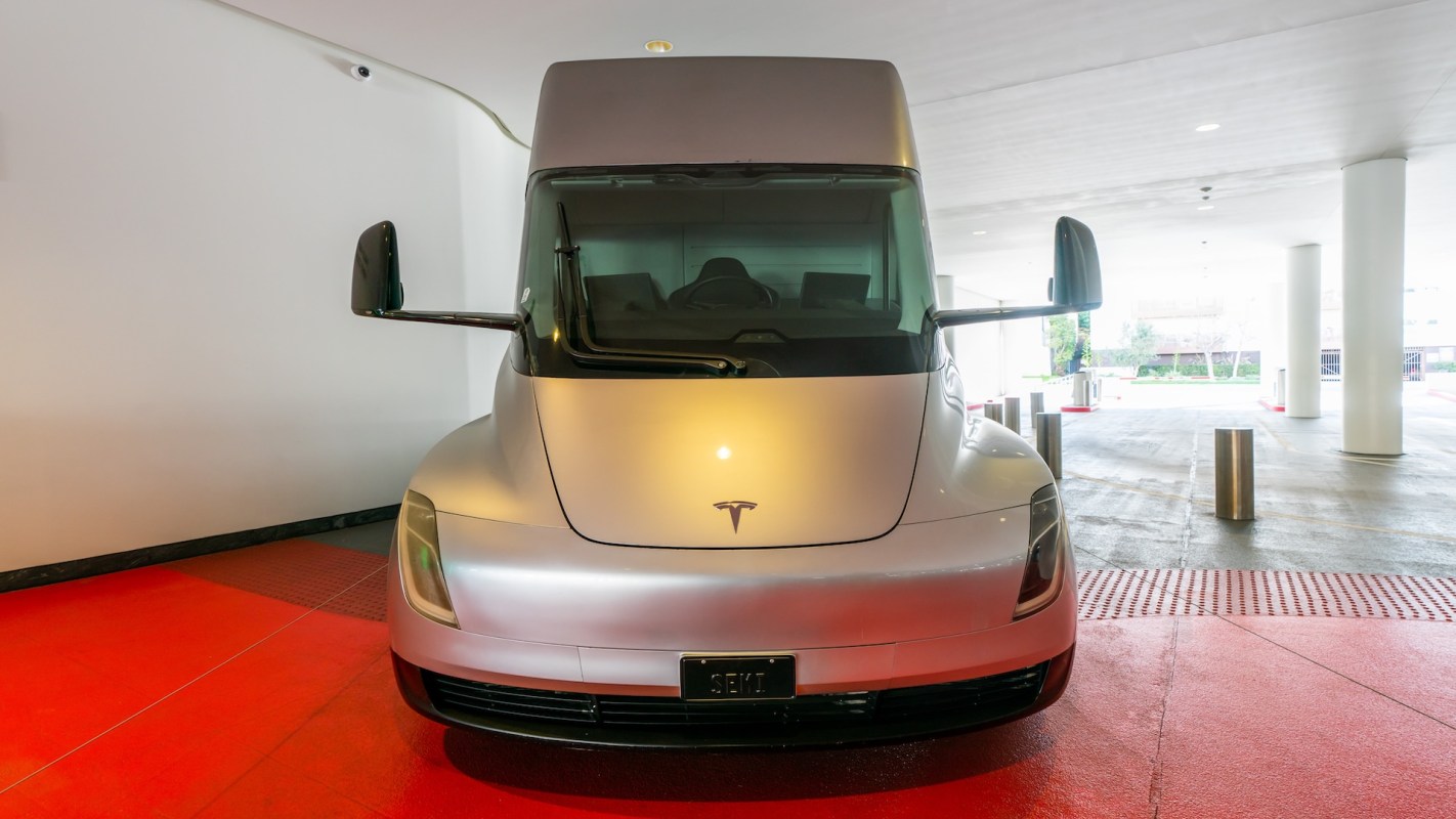 A Tesla semi-truck parked indoors, facing forward against a white wall.
