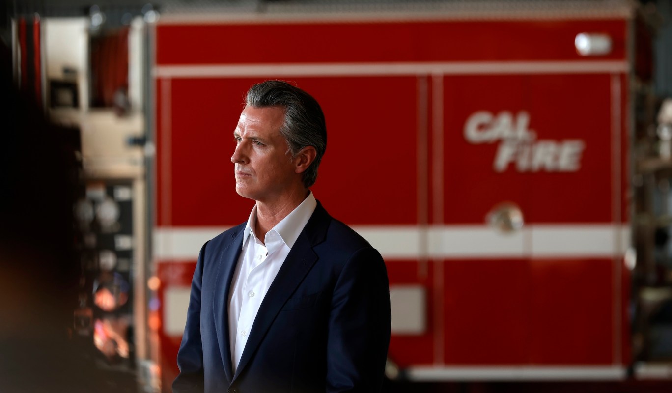 California Gov. Gavin Newsom stands in front of a red Cal Fire truck.