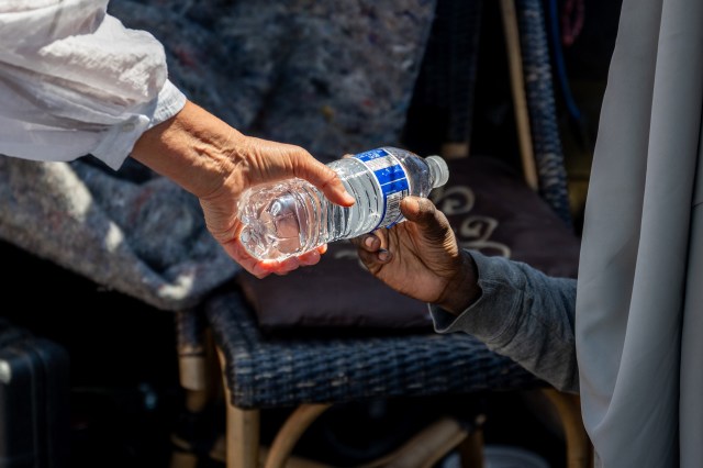 A hand passes a bottle of water to a homeless person.