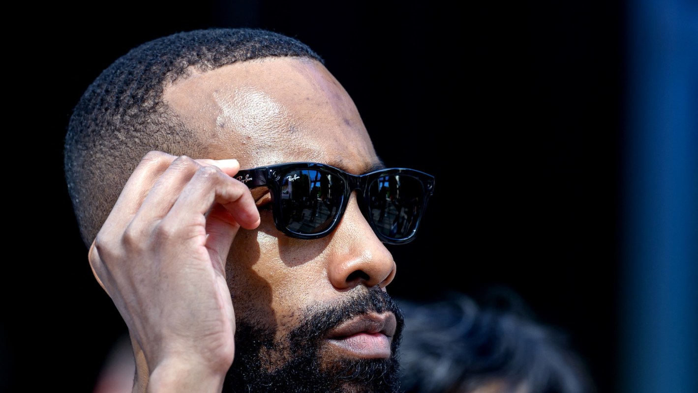 A man adjusts his Meta Ray-Ban sunglasses while standing outdoors.