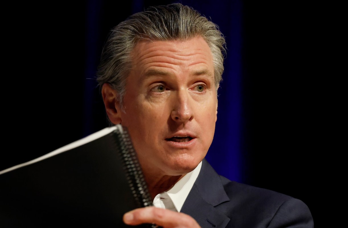 California Governor Gavin Newsom holds a spiral notebook and speaks at an event.