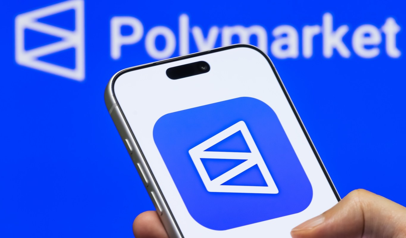 A smartphone displaying the Polymarket app logo against a blue background.