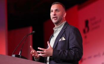 A speaker gestures while presenting at a podium during a conference.