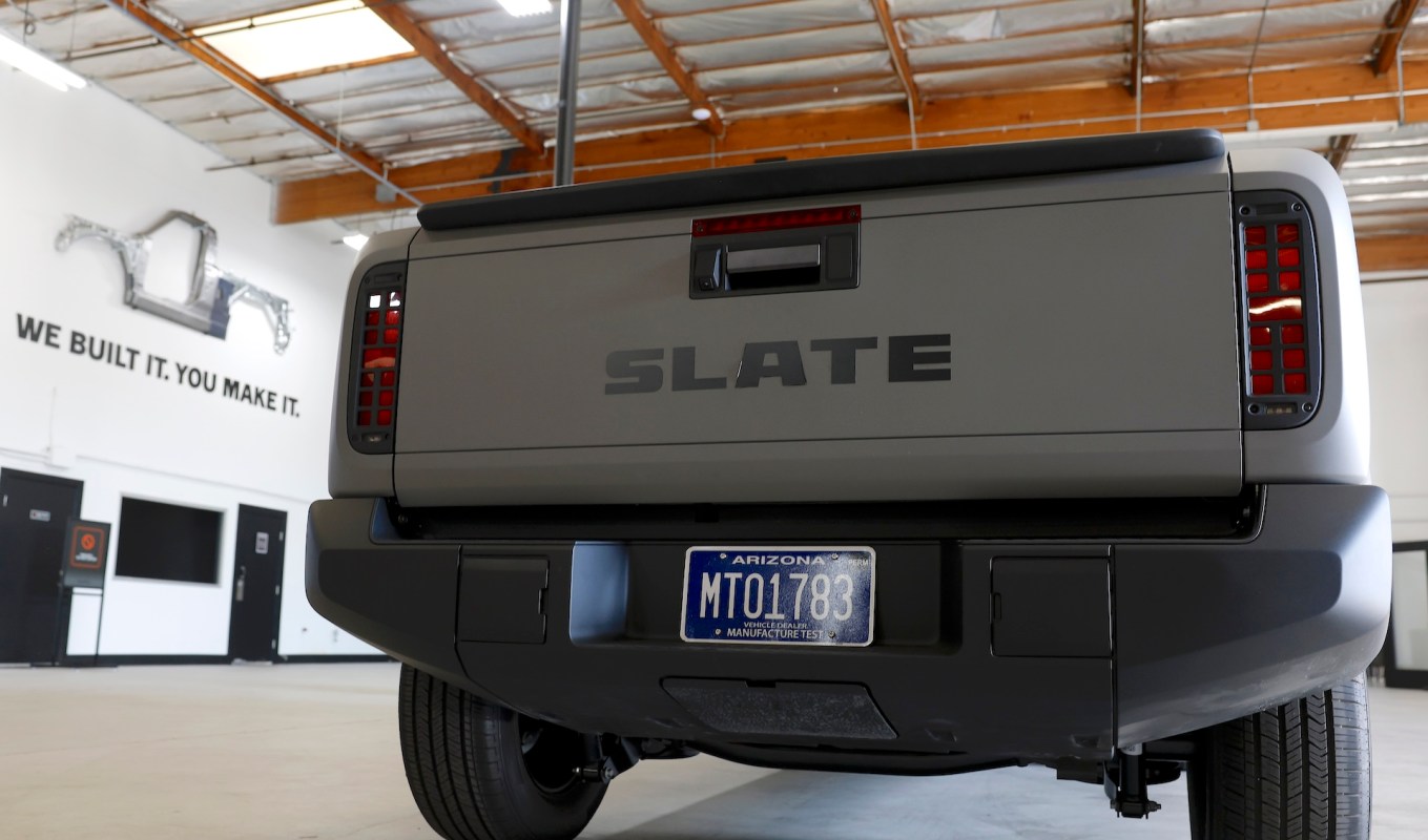 A gray vehicle with the word "SLATE" on the tailgate in a garage space with a wall sign.