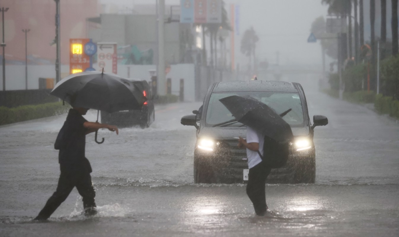Two people walk in a flooded street while a vehicle drives through the water during Typhoon Dujuan in Japan.