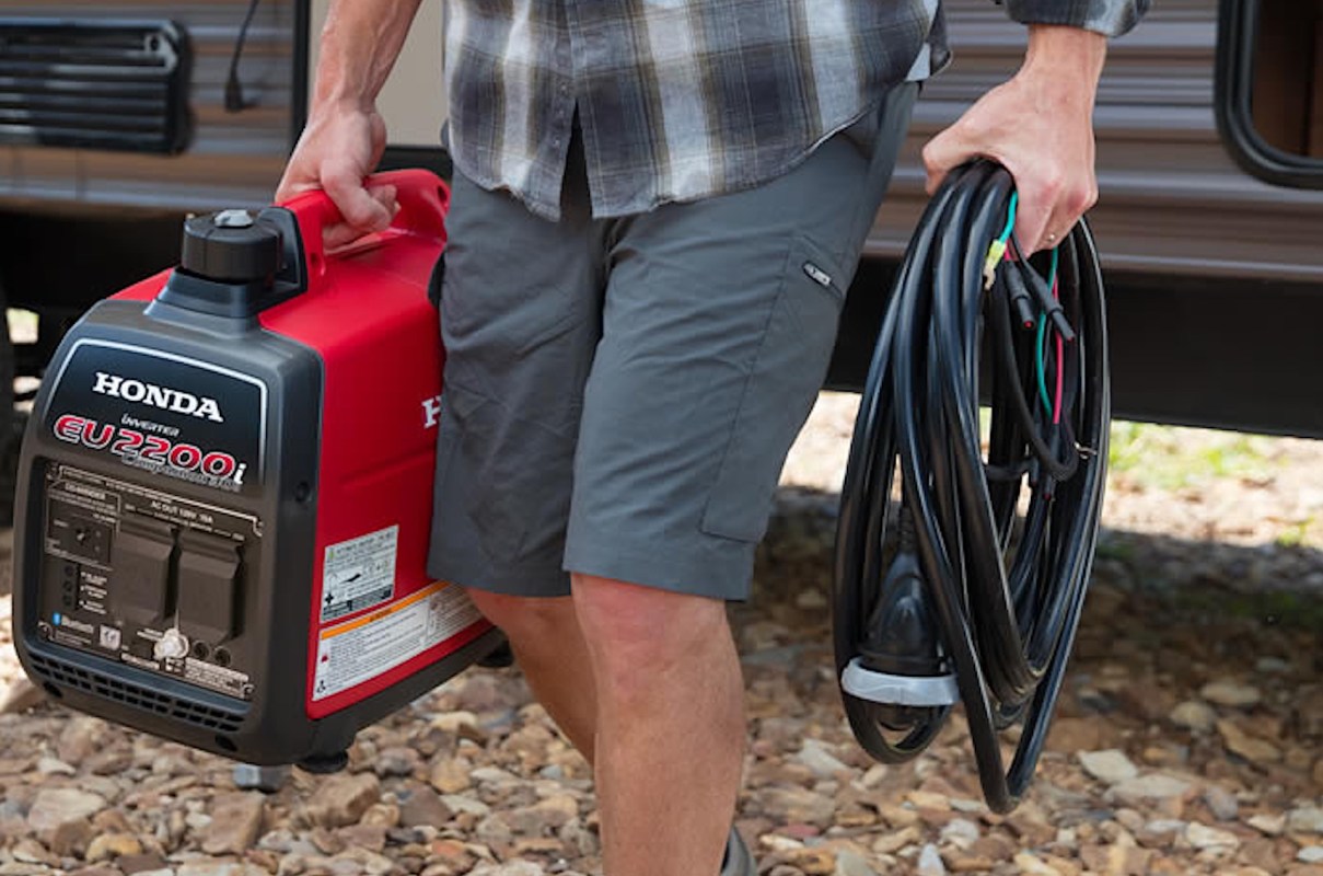 A person carries a Honda generator and a coil of electrical cables outdoors.