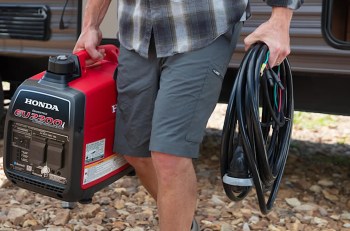 A person carries a Honda generator and a coil of electrical cables outdoors.