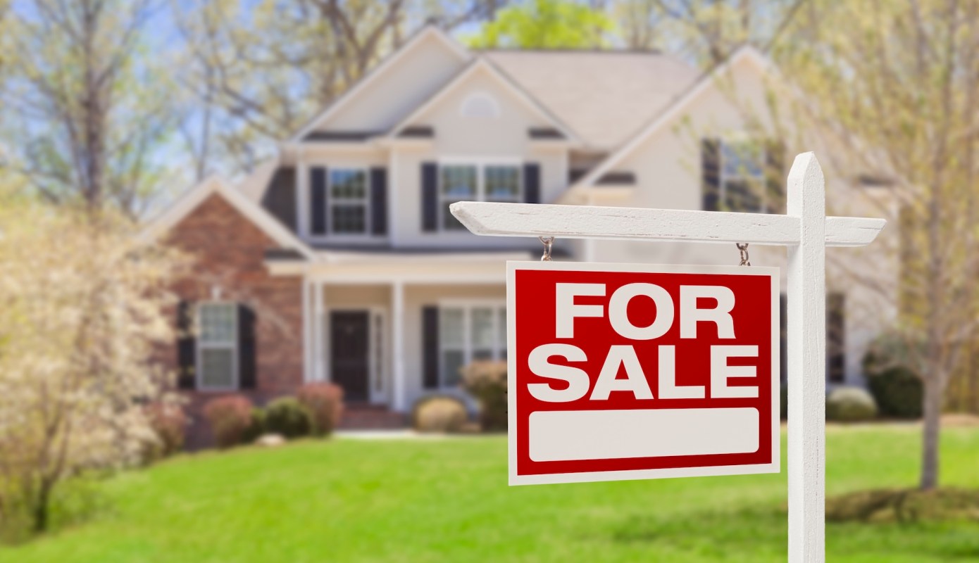 A house with a "For Sale" sign in front of a well-maintained lawn.