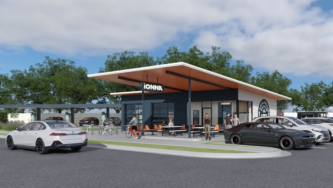 A modern Ionna restaurant building with orange accents and outdoor seating, surrounded by parked cars and greenery.