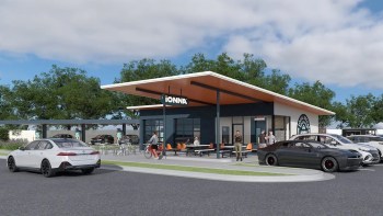 A modern Ionna restaurant building with orange accents and outdoor seating, surrounded by parked cars and greenery.