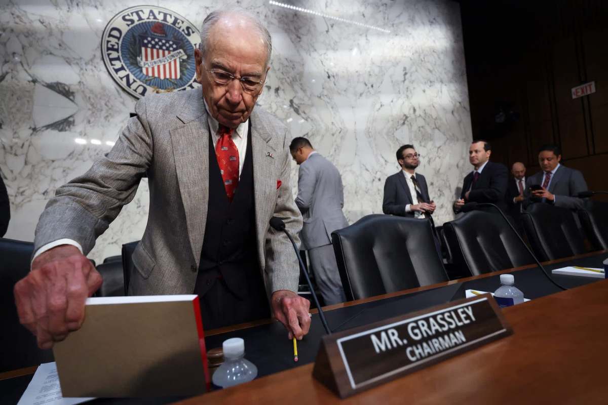 U.S. Senator Chuck Grassley adjusts a book on a table in a formal setting with other people in the background.