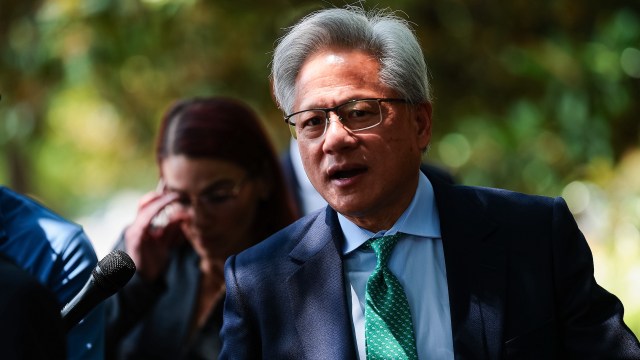 Nvidia CEO Jensen Huang speaks into a microphone, with another person partially visible in the background.