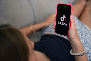 A teenage girl holds a cell phone in front of her displaying the TikTok app