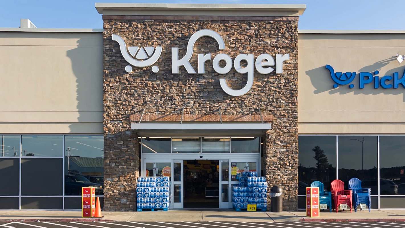 The entrance of a Kroger grocery store featuring a stone facade, shopping carts, and outdoor chairs.
