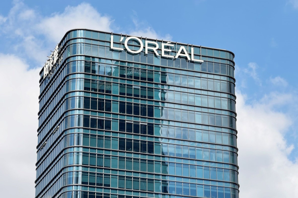 A modern glass building with the L'Oréal sign on top against a partly cloudy sky.