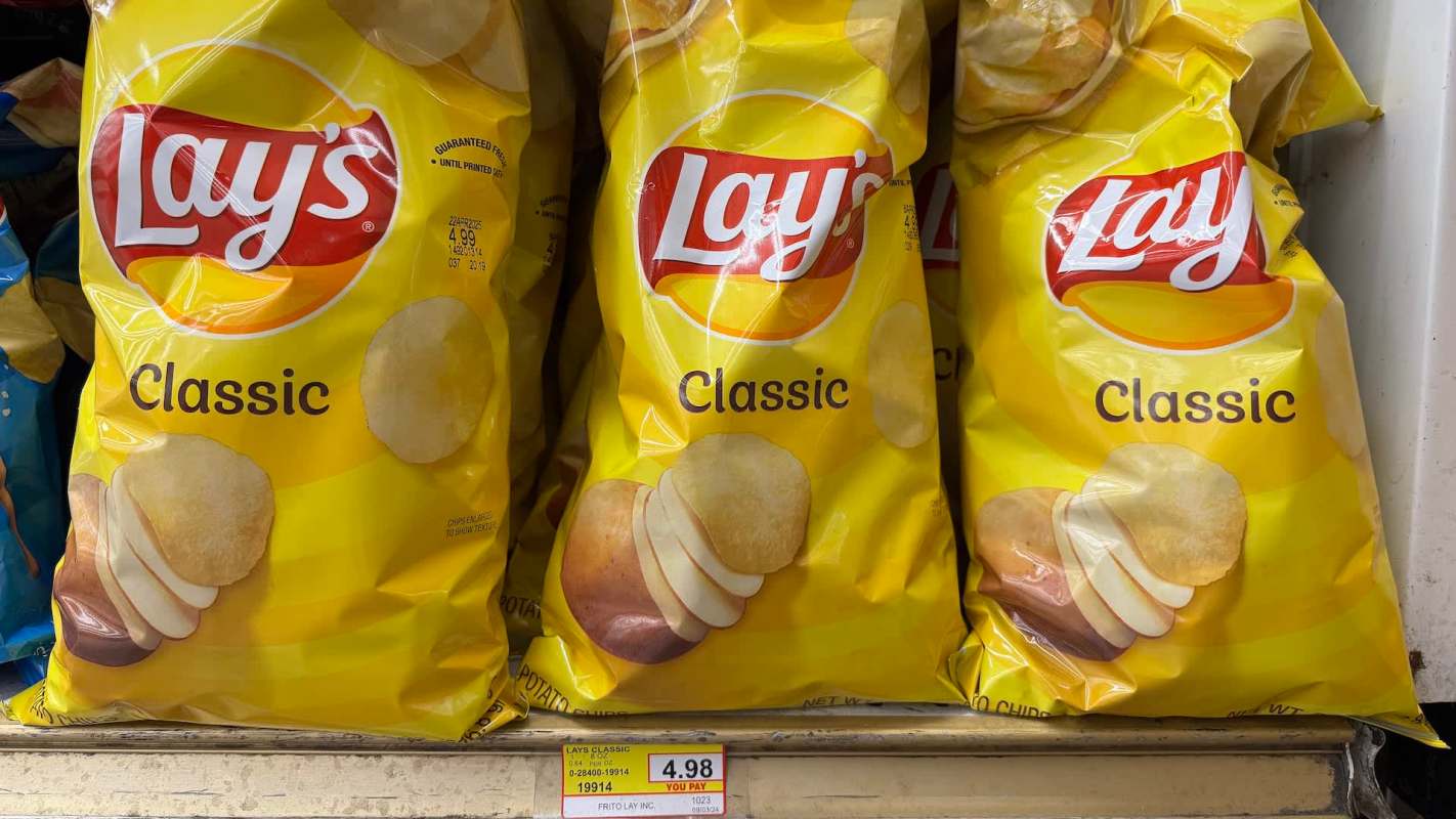 Three bags of Lay's Classic potato chips displayed on a shelf with a price tag of $4.98.